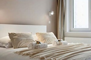 A neatly made bed with pillows and rolled towels, a window with curtains, and a wall-mounted light fixture. - Alejandro | Trendy apartment 30m from the beach in Ostend | Sleeps 8 (Oostende)