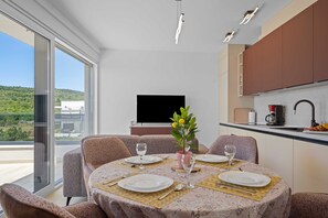 A dining area with a table set for four, a television in the background, and a view of greenery outside.
