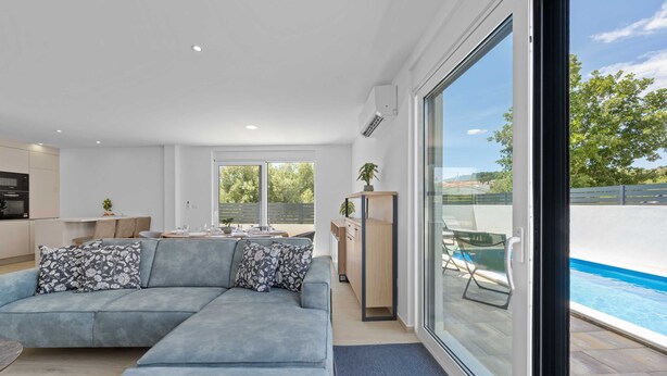 A modern living room with a sectional sofa, a dining area, and a view of a swimming pool. - Villa Jurić (Vodice)