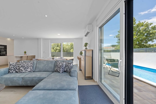 A modern living room with a sectional sofa, a dining area, and a view of a swimming pool.