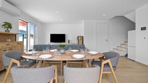 A modern dining area with a round table, grey upholstered chairs, and a television in the background. - Villa Jurić (Vodice)