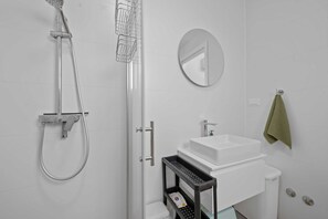 A modern bathroom with a shower, sink, mirror, and towel rack.