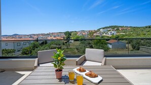 A balcony with a table, two chairs, a potted plant, and a tray with croissants and drinks. - Villa Jurić (Vodice)