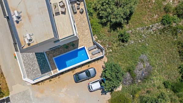 Vista aérea de una casa moderna con piscina, un coche y una entrada para vehículos.