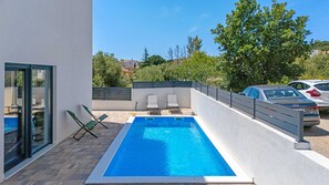 A rectangular swimming pool with two lounge chairs and a glass door on the left.