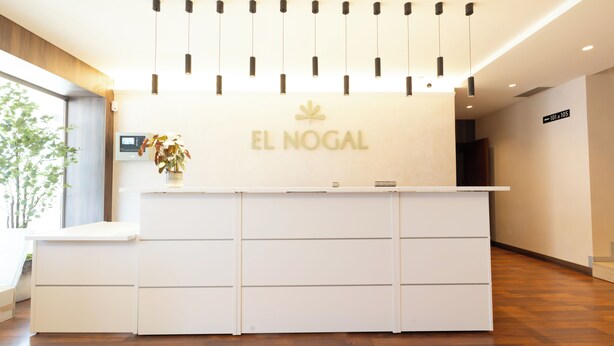 En receptionsdisk med et skilt der siger 'EL NOGAL', en moderne lysarmatur og en digital skærm.