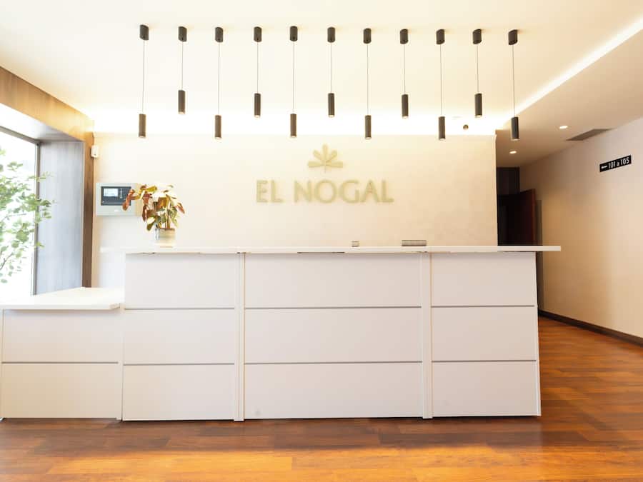 A reception desk with a sign reading 'EL NOGAL,' a modern light fixture, and a digital screen.
