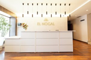 Un mostrador de recepción con un cartel que dice 'EL NOGAL', una lámpara moderna y una pantalla digital.