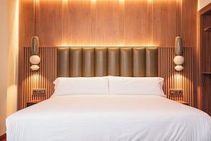 A large bed with a wooden headboard, two bedside tables with lamps, and a wall-mounted light fixture.