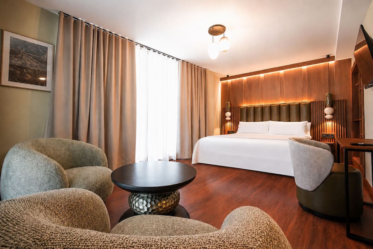 A hotel room with a bed, two armchairs, a small table, and a nightstand.