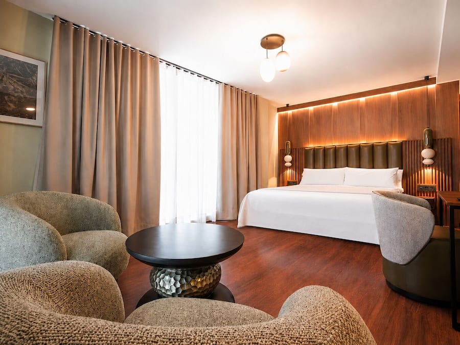 A hotel room with a bed, two armchairs, a small table, and a nightstand.