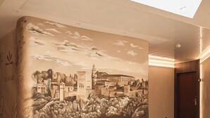 Et moderne interiør med en buet grøn sofa, et muralmaleri af et historisk bybillede og et ovenlysvindue.