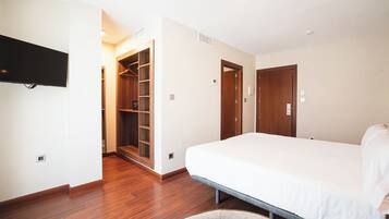 Una habitación de hotel con cama, televisor montado en la pared, piso de madera y vestidor.