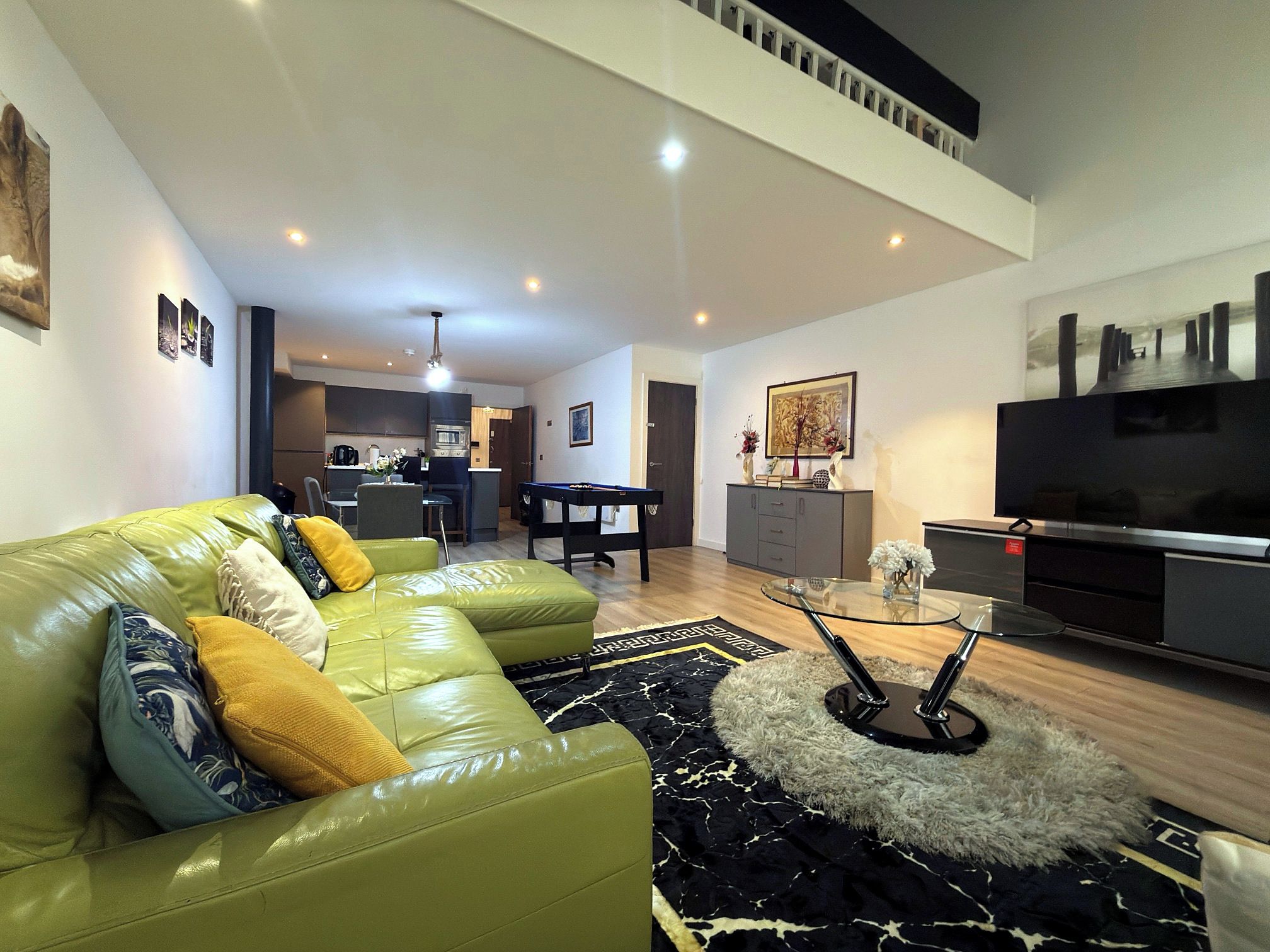 A modern living room with a green sofa, a glass coffee table, and a flat-screen TV.