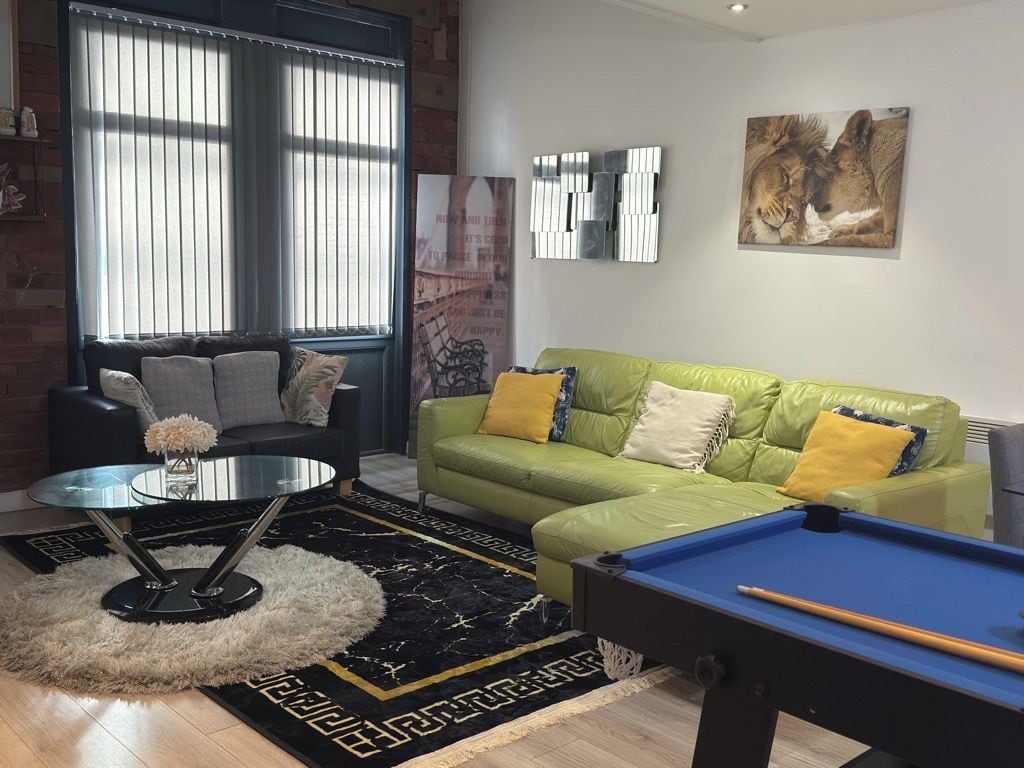 A living room with a pool table, green sofa, and a large window with blinds.