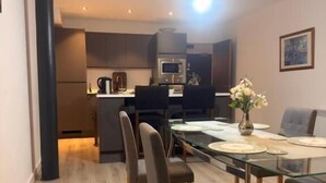 A modern dining area with a glass table, chairs, and a vase of flowers. - Modern Bradford City Apartment Steps From Stadium and Train Station (Bradford)
