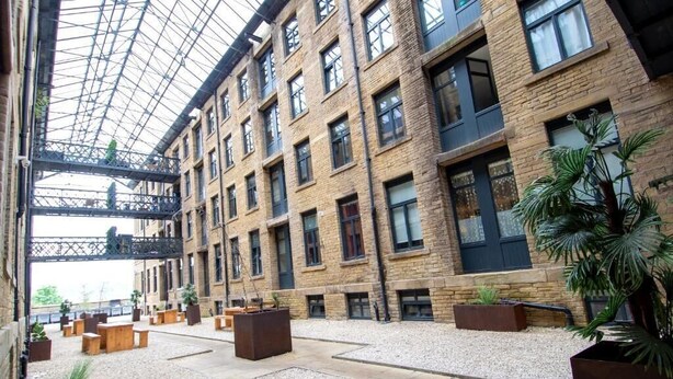 A spacious atrium with a high ceiling, multiple floors, and a central open area with seating and planters. - Modern Bradford City Apartment Steps From Stadium and Train Station (Bradford)
