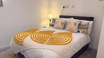 Un dormitorio con cama, mesita de noche, lámpara y enchufe.