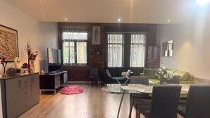 A modern dining area with a glass table, chairs, a sofa, and a TV. - Modern Bradford City Apartment Steps From Stadium and Train Station (Bradford)