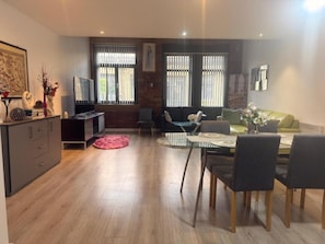 Ein stilvoller Essbereich mit einem Glastisch, Stühlen, einer Couch und einem Fernseher.
