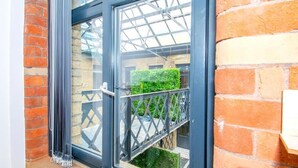 A window with a metal frame, a brick wall, and a view of a green hedge. - Modern Bradford City Apartment Steps From Stadium and Train Station (Bradford)