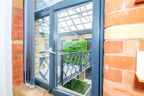 Ein Fenster mit Metallrahmen, eine Ziegelwand und Blick auf einen grünen Heckenstreifen.