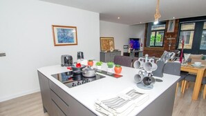 A modern kitchen with a central island, a dining area with a wooden table, and a living space with a TV and seating. - Modern Bradford City Apartment Steps From Stadium and Train Station (Bradford)