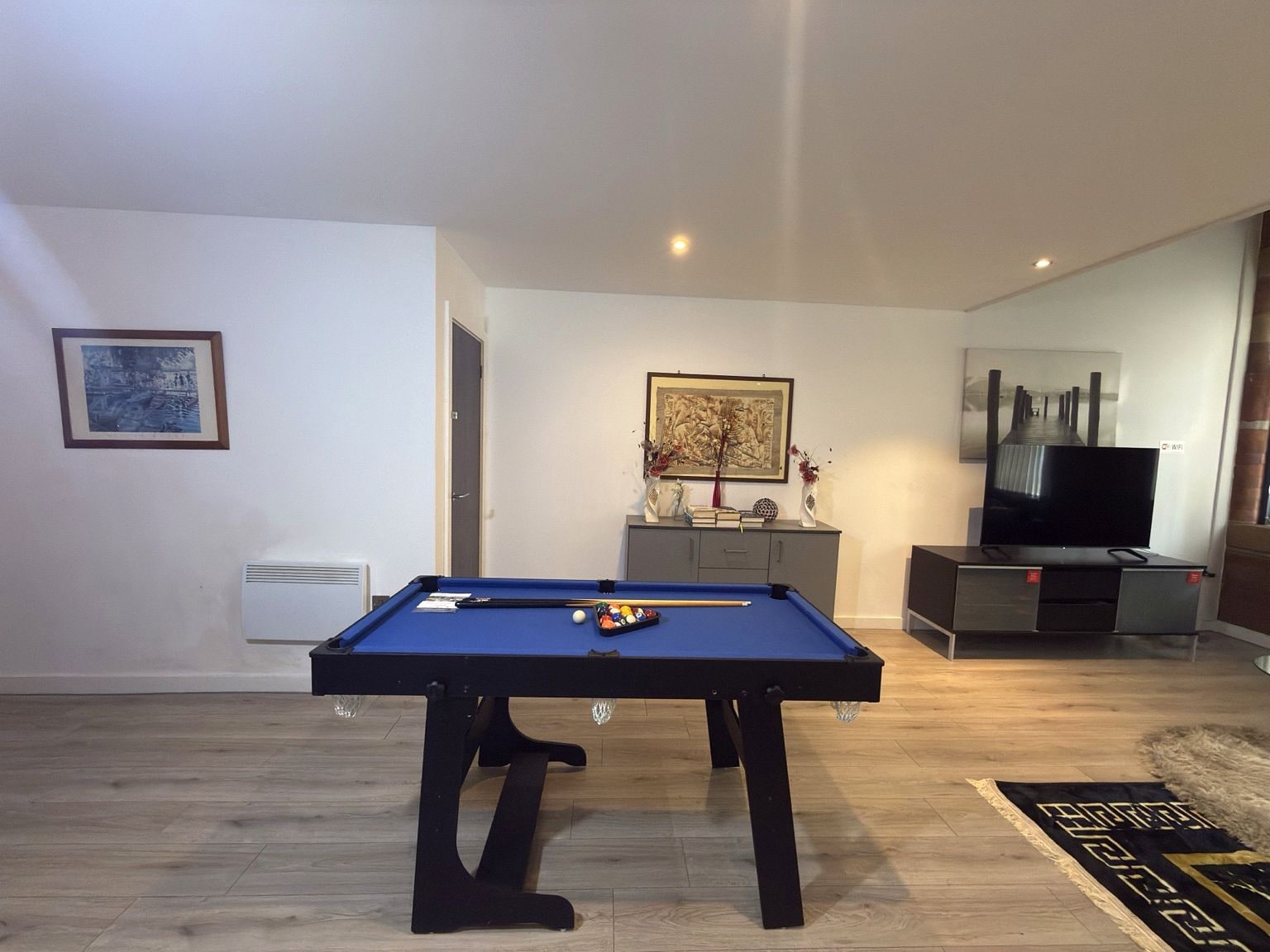 A room with a pool table, a television, and a cabinet with decorative items.