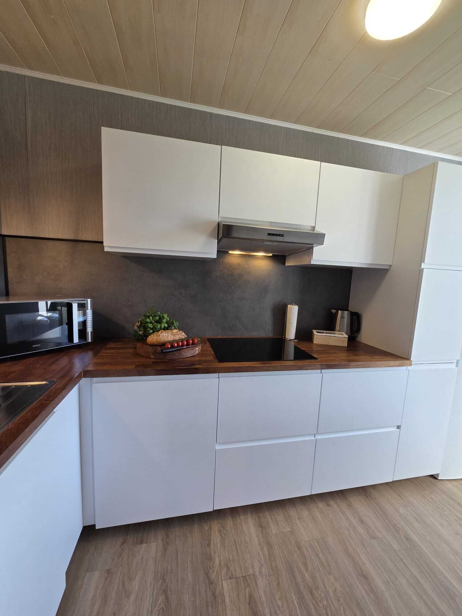 A modern kitchen with white cabinetry, a wooden countertop, a built-in microwave, and a stainless steel range hood.