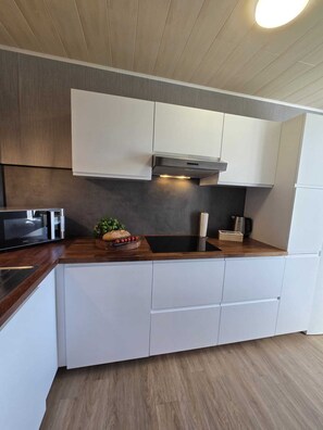Een moderne keuken met witte kastjes, een roestvrijstalen afzuigkap, een inbouwmagnetron en een houten aanrecht.
