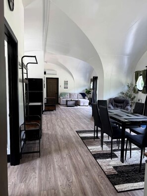 A spacious living area with a high ceiling, a dining table with chairs, a sofa, and a coffee table.