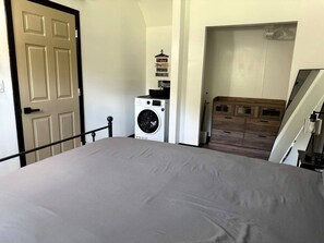 Un dormitorio con cama, lavadora y cómoda de madera.