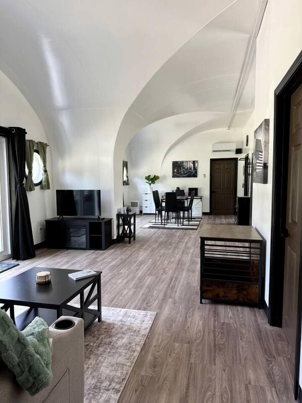 A spacious living area with a TV, dining table, and chairs, leading to a kitchen and dining area.