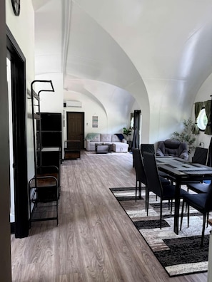 A spacious living area with a high ceiling, a dining table with chairs, a sofa, and a coffee table.
