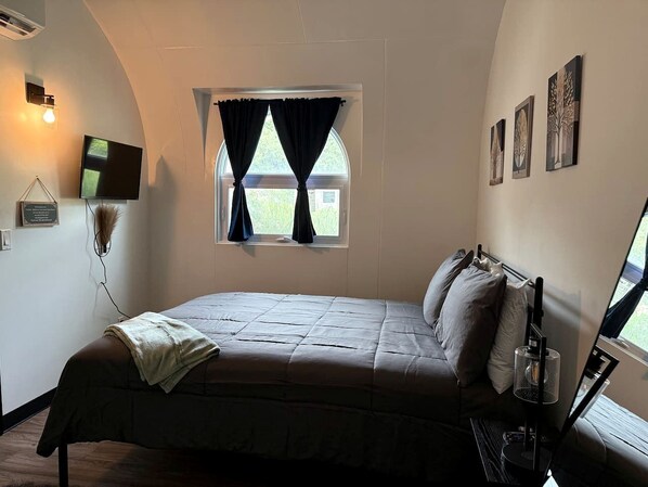 A bedroom with a bed, a window with curtains, a flat-screen TV, and wall-mounted artwork.