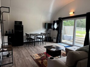 Un espace de vie compact comprenant un coin repas, un canapé, un téléviseur et une porte-fenêtre coulissante donnant sur un espace extérieur.