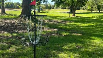 A disc golf basket in a park with trees and grass.