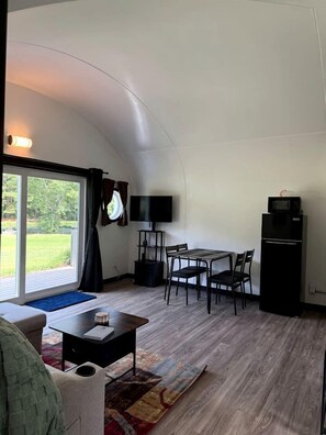 A compact living space with a dining area, a flat-screen TV, a black refrigerator, and a large sliding glass door leading to an outdoor area.