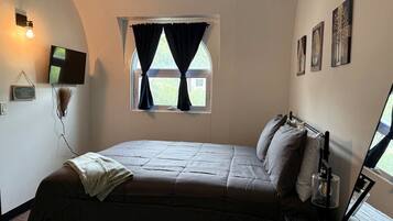 A bedroom with a bed, a window with curtains, a flat-screen TV, and wall-mounted artwork.