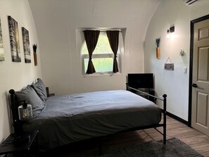 A bedroom with a bed, a TV, a window with curtains, and a door.