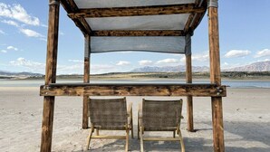 A wooden structure with a canvas roof, two wicker chairs, and a view of a lake and mountains.