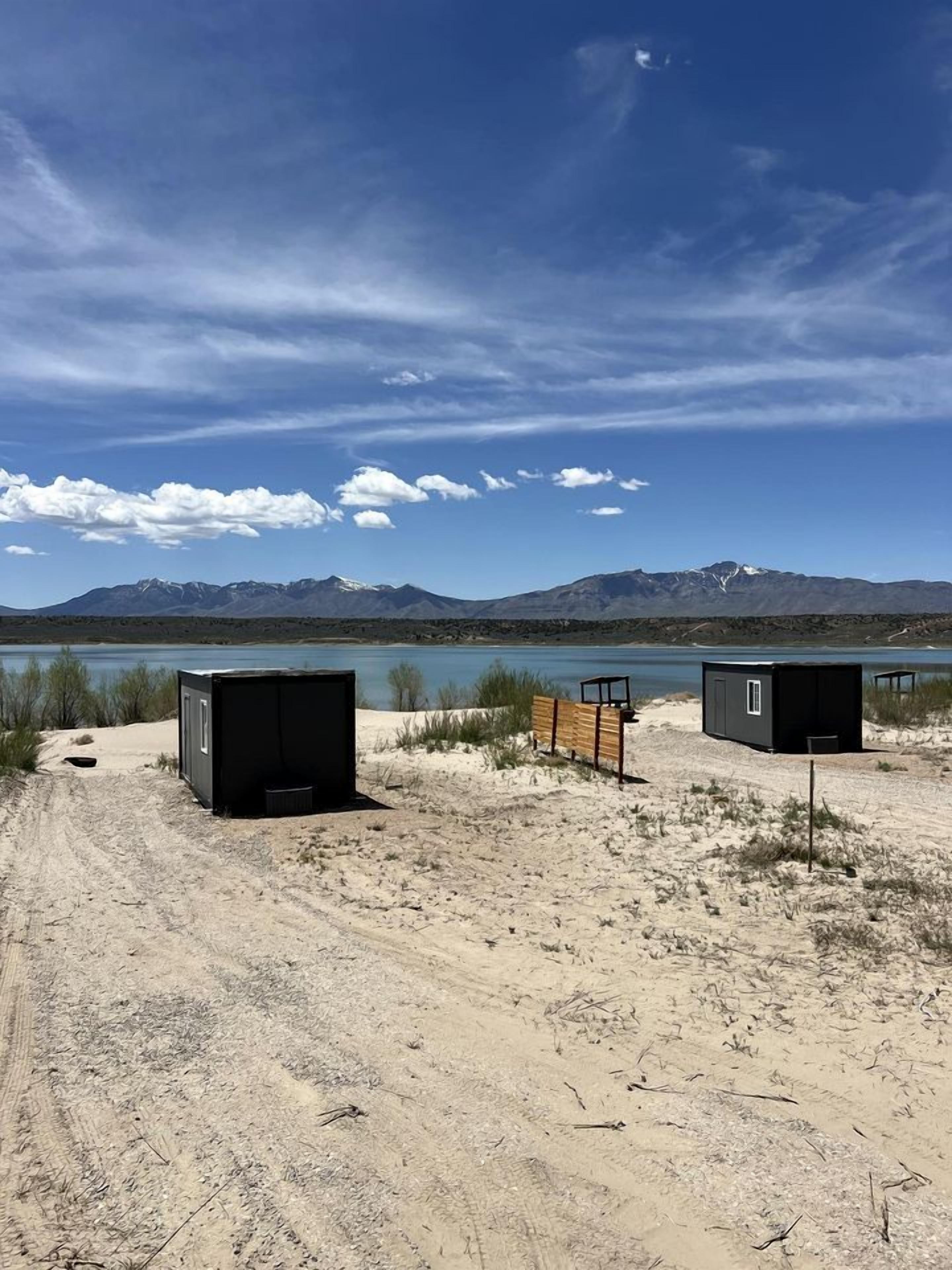 Paisaje desértico con dos cabañas pequeñas y oscuras, y un banco de madera.