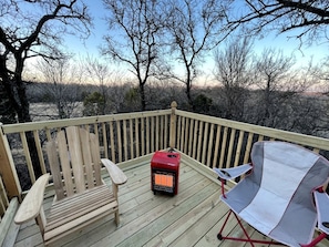 A wooden deck with a chair, a small heater, and a folding chair.