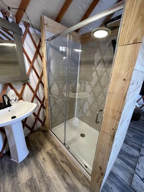 Une salle de bain avec une douche à parois de verre, un lavabo blanc et des poutres en bois.