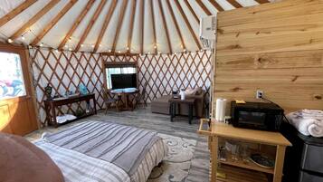 Interieur van een joert met een bed, zithoek, tafel en een televisie.
