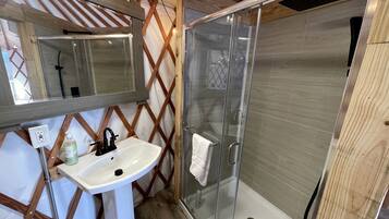 A bathroom with a glass shower enclosure, a sink with a mirror, and wooden beams.