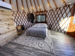 Une pièce chaleureuse avec un lit, un mur en bois, une fenêtre avec des stores et une guirlande lumineuse.