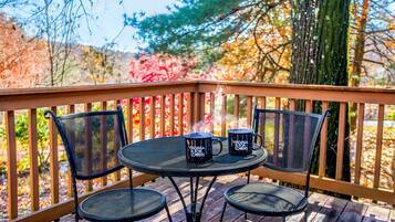 Une terrasse en bois avec une table ronde et deux chaises, entourée d’une rambarde.