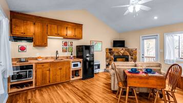 A kitchen with wooden cabinets, a black refrigerator, a stone fireplace, and a dining area with a table and chairs.