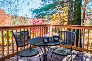 Une terrasse en bois avec une table ronde et deux chaises, entourée d’une rambarde.